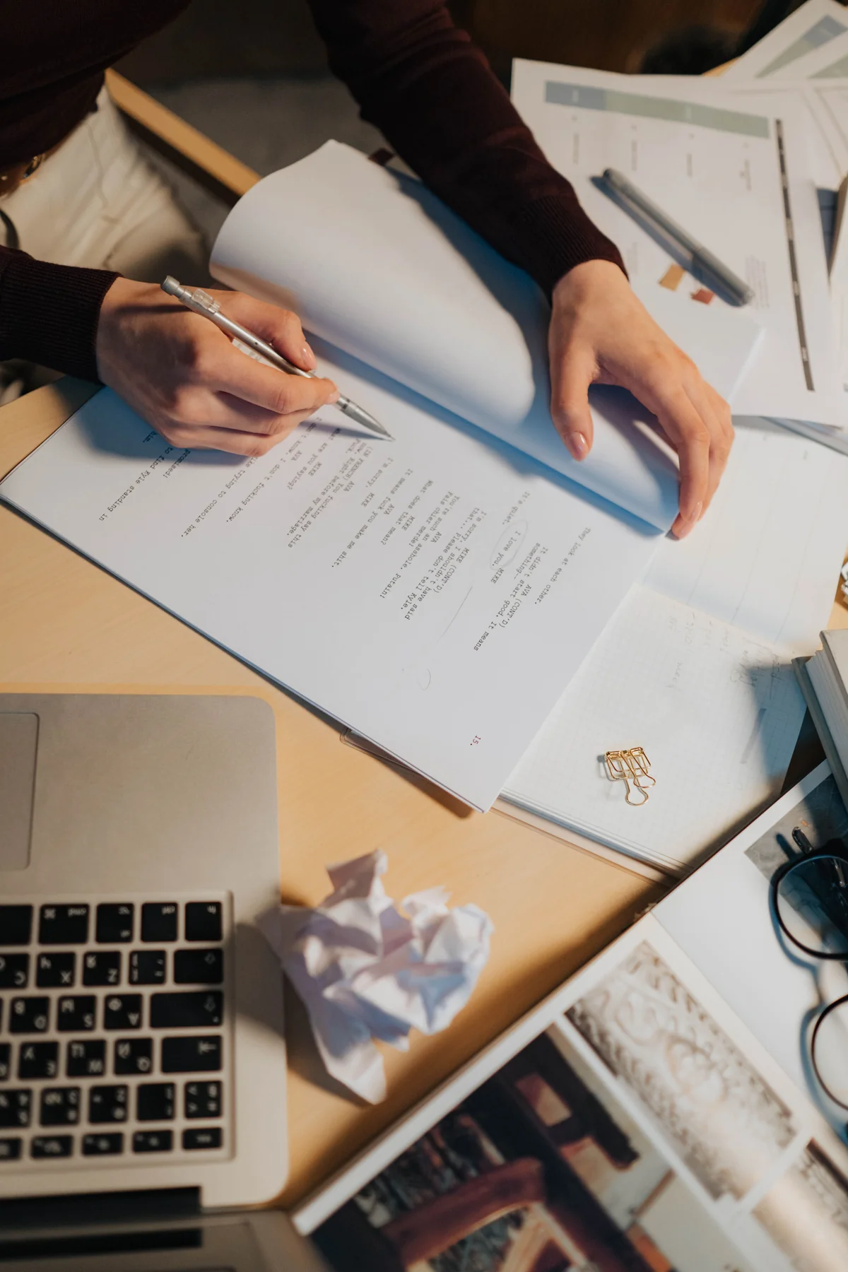 Hands annotating printed pages beside a laptop